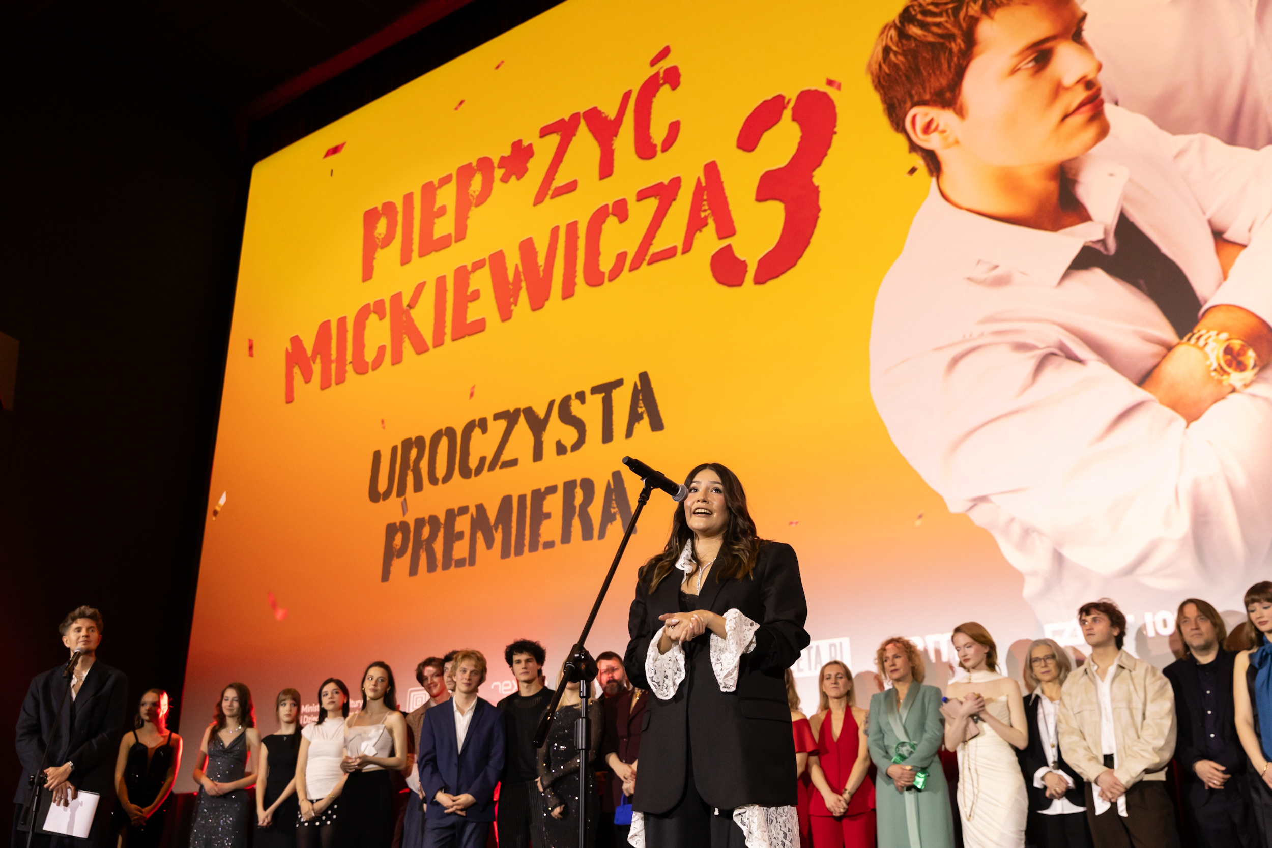 Reżyserka Sara Bustamante-Drozdek przemawia na scenie podczas uroczystej premiery, za nią stoi cała obsada filmu